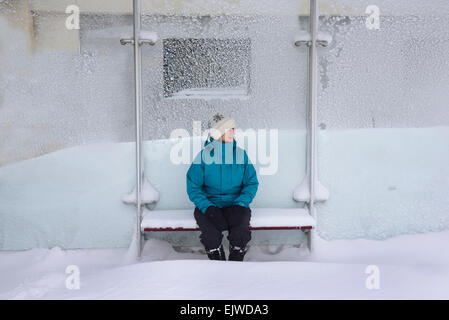 USA, Massachusetts, Boston, Middle aged woman sitting in bus stop, winter snow Stock Photo