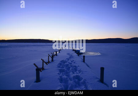 USA, New York, Lake George, Symmetrical image of snowed jetty with footprints at dawn, hills on horizon Stock Photo