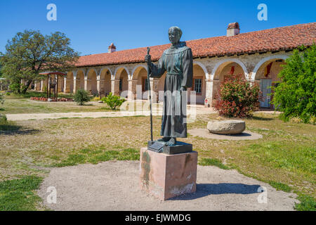 Bronze statue of Fr. Junipero Serra in front of the red tile roof and multiple arches of the Mission San Antonio de Padua. Stock Photo