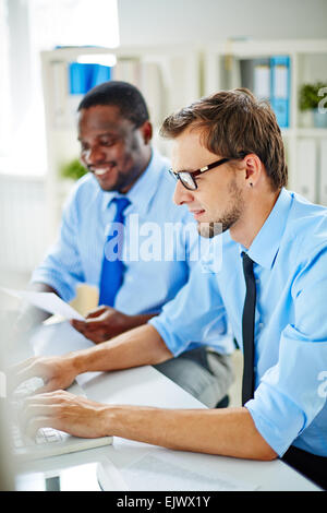Young office worker typing on background of his colleague Stock Photo
