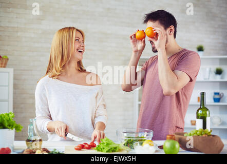 Happy young woman cooking salad while her husband making fun near by Stock Photo