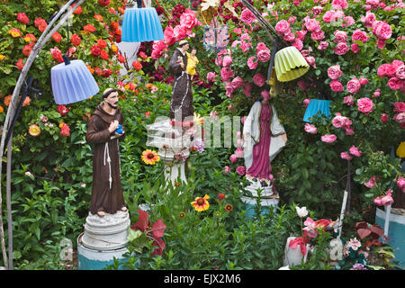 Religious figurines and June bright June blooming roses create a quirky but beautiful diorama at the garden of C. L. 'Tunnie'. Stock Photo