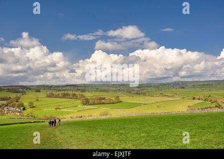 White Peak landscape on a sunny spring day with fluffy clouds above green farmland. Walkers on a footpath across a field.