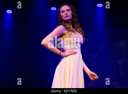 Woman with long curly hair and red lipstick wearing a long white dress posed at a fashion showcase on a catwalk. Stock Photo