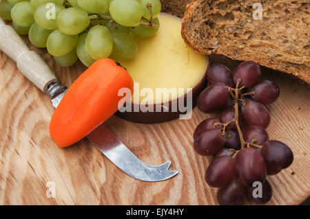 cheese, bread and grapes on wooden cutting board Stock Photo