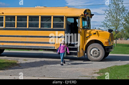 Young Caucasian girl getting off a yellow school bus. Stock Photo