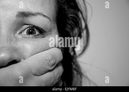 Close up portrait of a young scared woman being abused by someone in monochrome indoors Stock Photo