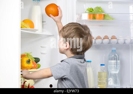 Little cute boy picking orange from fridge Stock Photo