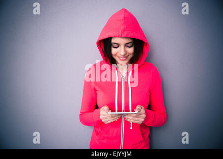 Beautiful cute woman using smartphone over gray background. Looking on smartphone. Wearing in pink jacket Stock Photo