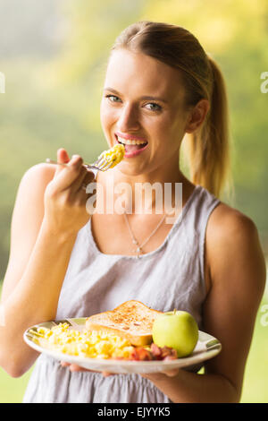 happy young woman eating scrambled eggs for breakfast Stock Photo