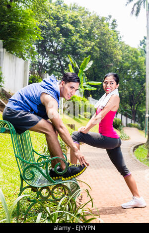 Woman and man, an Asian couple, exercising for fitness sport in tropical park on bench Stock Photo