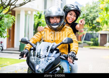 Couple with helmets riding motorcycle, wife is sitting behind her husband Stock Photo