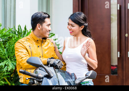 Woman saying goodbye to motorcyclist who is riding off to work in the morning Stock Photo