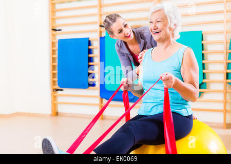 Senior woman with stretch band in fitness gym being coached by personal trainer Stock Photo