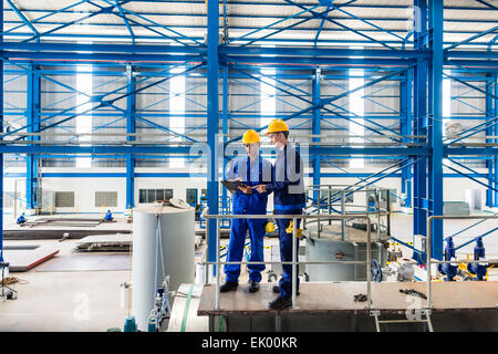 Two workers in large metal workshop or factory checking work standing on large machine Stock Photo