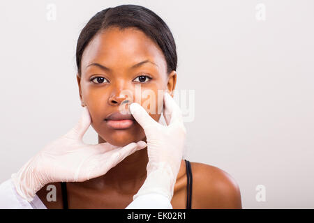 doctor checking African woman lips before plastic surgery on plain background Stock Photo