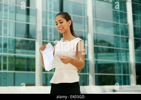 Portrait of beautiful latina businesswoman resigns from job, tearing an employment contract and smiling. The lady is standing in Stock Photo