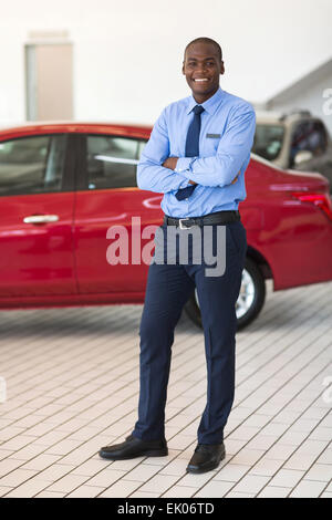 good looking African vehicle salesman with arms crossed standing in showroom Stock Photo