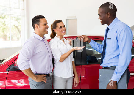 car salesman handing over new car key to couple in car showroom Stock Photo