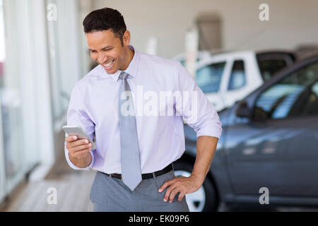 happy car salesman using smart phone in showroom Stock Photo