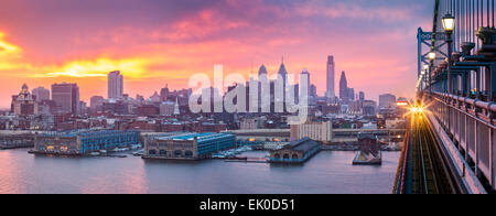 Philadelphia panorama under a hazy purple sunset. An incoming train crosses Ben Franklin Bridge. Stock Photo