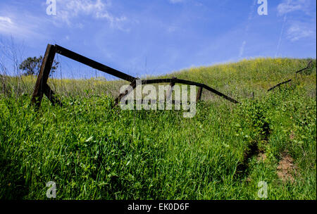 Old, broken down fence on a grassy hill against a blue sky. The fence goes up and over the hillside. Stock Photo
