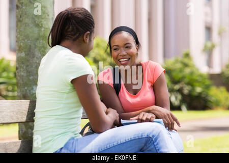 cheerful African female students sitting on bench at university campus Stock Photo