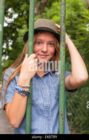 Young girl standing behind the bars of the old park. Stock Photo