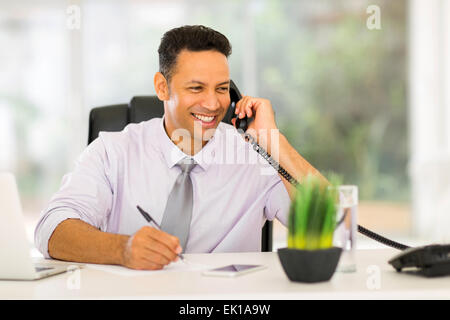 smiling middle aged businessman talking on landline phone and writing report Stock Photo
