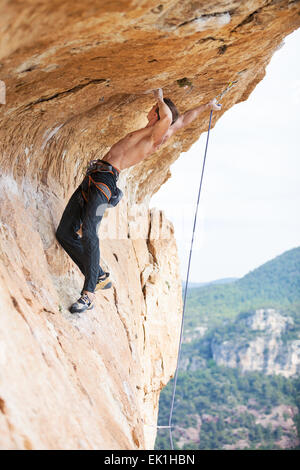 Young man clipping rope while clinging to cliff under ledge, challenging part of route Stock Photo