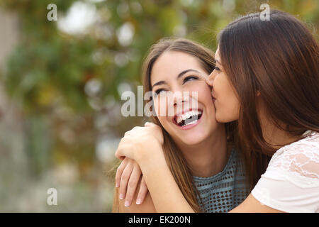 Two funny affectionate women friends laughing and kissing outdoors Stock Photo