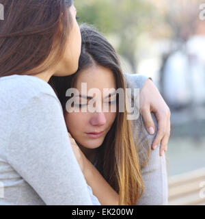 Sad girl crying and a friend comforting her outdoors in a park Stock Photo