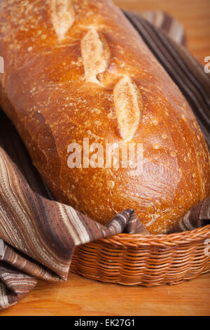 Loaf of homemade sourdough bread in a bread basket lined with a brown striped tea towel Stock Photo