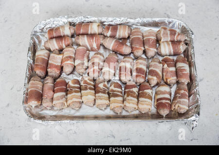 Tray lined in foil with uncooked small sausages wrapped in bacon (pigs in blankets) ready for cooking, part of a traditional Christmas lunch or dinner Stock Photo