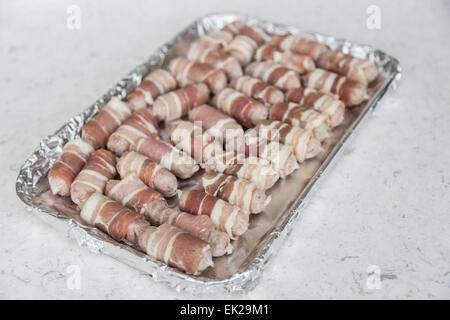 Tray lined in foil with uncooked small sausages wrapped in bacon (pigs in blankets) ready for cooking, part of a traditional Christmas lunch or dinner Stock Photo