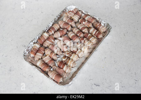 Tray lined in foil with uncooked small sausages wrapped in bacon (pigs in blankets) ready for cooking, part of a traditional Christmas lunch or dinner Stock Photo