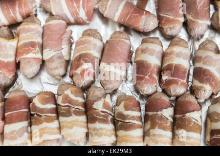 Tray lined in foil with uncooked small sausages wrapped in bacon (pigs in blankets) ready for cooking, part of a traditional Christmas lunch or dinner
