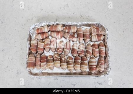 Tray lined in foil with uncooked sausages wrapped in bacon (pigs in blankets) ready for cooking Stock Photo
