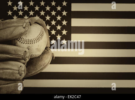 vintage concept of worn leather mitt and used baseball with United States of America flag in background. Stock Photo