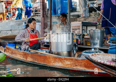 Thai woman prepares food in a boat at the Floating Market in Damnoen Saduak. The floating market is a major tourist attraction. Stock Photo