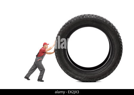 Full length portrait of a mechanic in a gray jumpsuit pushing a giant black tire isolated on white background Stock Photo