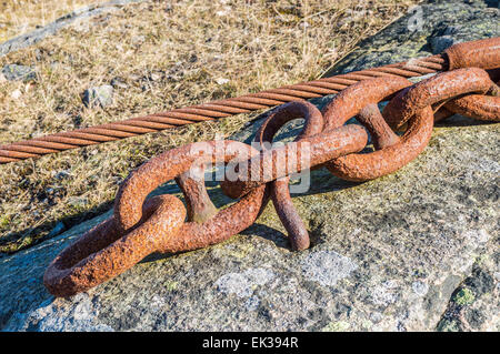 Old rusty chain and wire set in the rock to anchor heavy equipment. Stock Photo