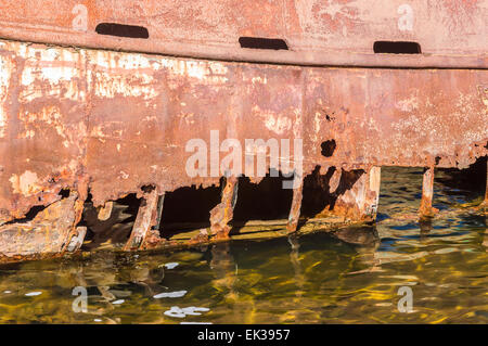 Detail of rusty hull with large holes. Water in foreground and inside shipwreck. Stock Photo