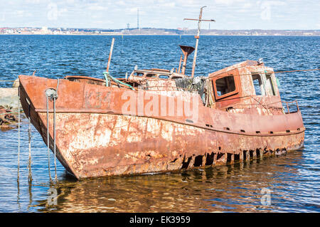 Front and side view of very rusty shipwreck with big holes in the hull. Still in water with the ocean in background. Stock Photo