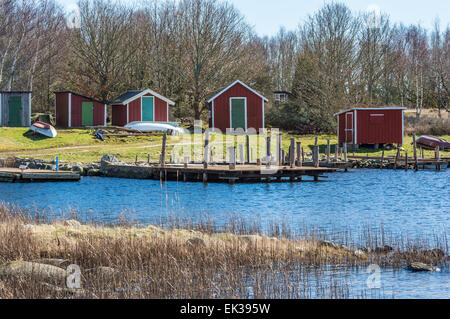 Red wooden boat houses with wooden bridges in front. Ocean and dry vegetation in foreground. Sunshine in early spring. Up side d Stock Photo