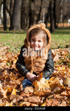 girl in a fur jacket sits on the fallen-down autumn leaves Stock Photo