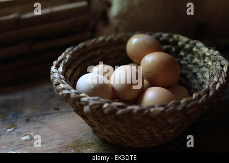 basket of eggs on wooden table illuminated by window / canasta de huevos, en mesa de madera iluminada por ventana Stock Photo