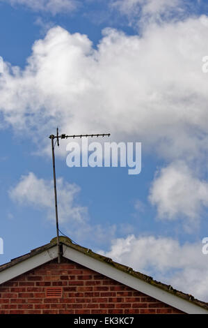 Basic television aerial/antenna on the roof of a house against blue sky with white clouds. Stock Photo