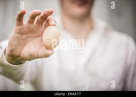 Farmer Showing an Egg in front of the Farm Stock Photo