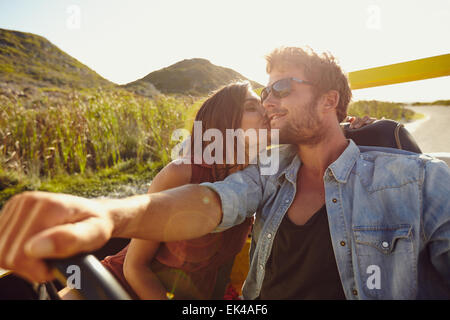 Woman kissing her boyfriend driving a car. Lovely young couple on road trip. Affectionate caucasian couple enjoying road trip. Stock Photo